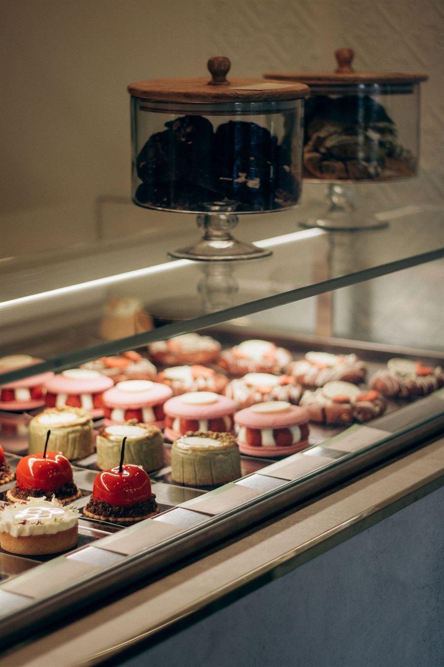Vitrine com doces finos, macarons gigantes e cerejas de chocolate, e potes de vidro com cookies
